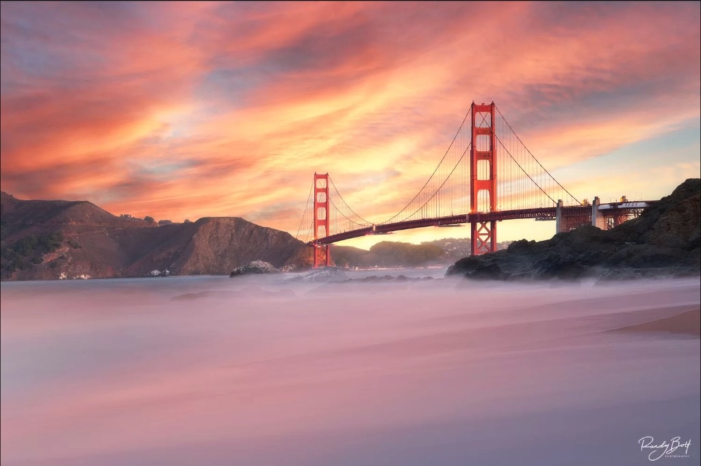 Golden Gate Bridge at sunset with vibrant orange and pink clouds and misty water