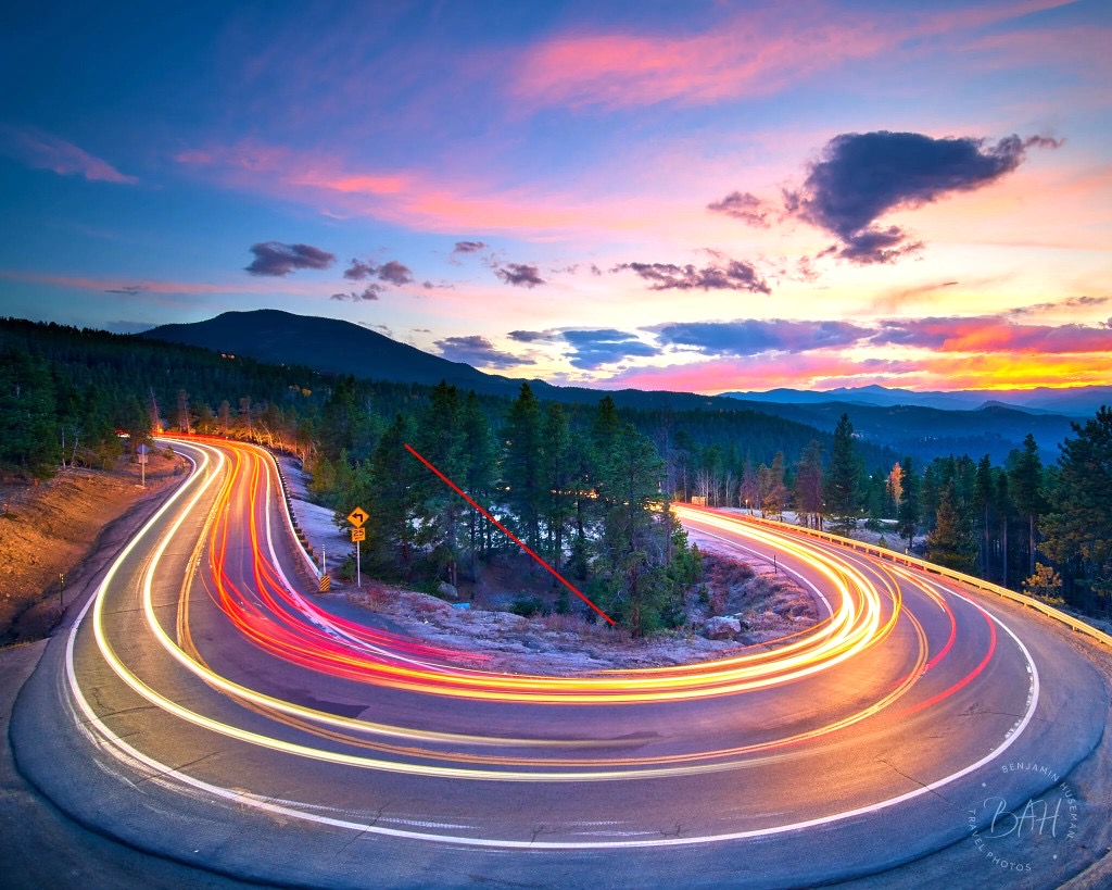Mountain road at sunset with light trails, illustrating speed and momentum